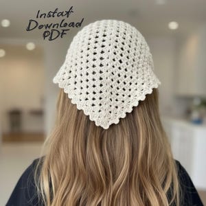 May include: A cream-colored, crocheted head covering with a square shape and scalloped edges. The text "Instat Download PDF" is written in cursive on the image. The head covering is worn on the head.