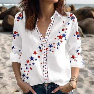 May include: White button-down shirt with a V-neck, adorned with red and blue star patterns. The stars are scattered across the shirt and along the button line. The shirt has long sleeves and is made of a lightweight fabric.