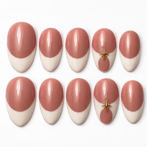 Peut inclure: Un ensemble de dix faux ongles en forme d'amande avec une base mauve brillante et une pointe française crème. Deux des ongles sont ornés d'une petite breloque en forme d'étoile dorée à quatre branches centrée sur la transition des couleurs.