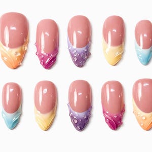 Pode incluir: Um conjunto de dez unhas postiças com base nude e pontas francesas coloridas em tons de laranja, rosa, roxo, amarelo e azul. Cada ponta é decorada com um padrão de redemoinho em relevo e pequenas gotas de água transparentes.