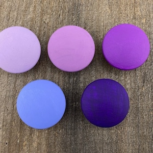 Może przedstawiać: Pięć okrągłych drewnianych guzików w odcieniach fioletu i lawendy. Guziki są ułożone w rzędzie od najjaśniejszego do najciemniejszego.