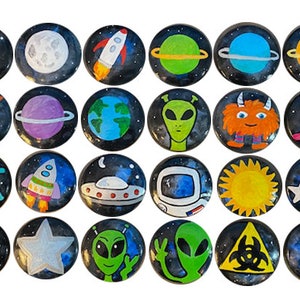 May include: A collection of 25 round, hand-painted magnets with space-themed designs. Each magnet features a different illustration, including planets, rockets, aliens, and celestial bodies, set against a dark, starry background.