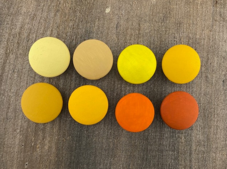 May include: Eight round wooden discs painted in shades of yellow, orange, and brown. The discs are arranged in two rows of four, with the lightest shade at the top and the darkest shade at the bottom.