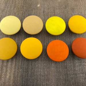 May include: Ten round wooden discs painted in shades of yellow, orange, and brown. The discs are arranged in two rows of five.