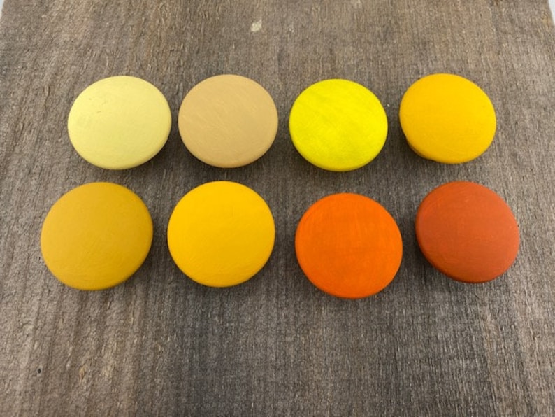 May include: Ten round wooden discs painted in shades of yellow, orange, and brown. The discs are arranged in two rows of five.