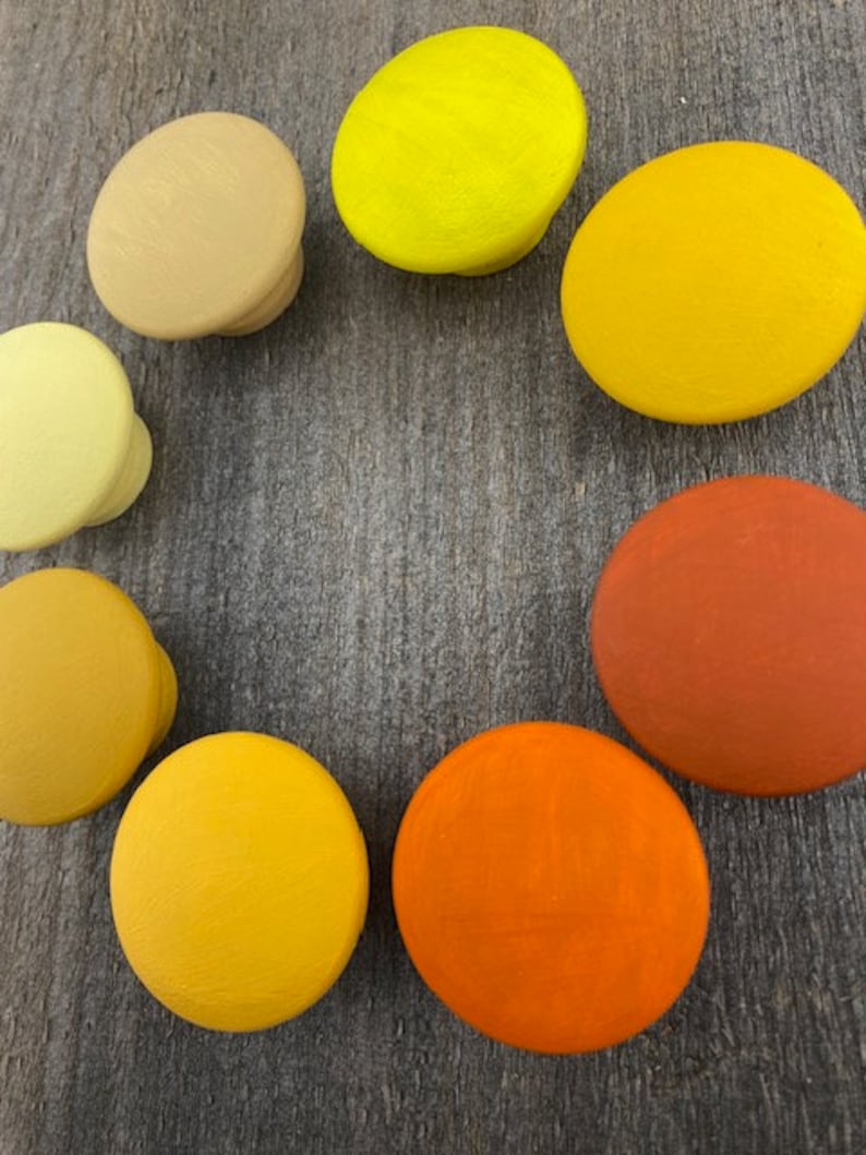 May include: Set of ten round wooden knobs in various shades of yellow and orange. The knobs are painted in a smooth, solid colour.