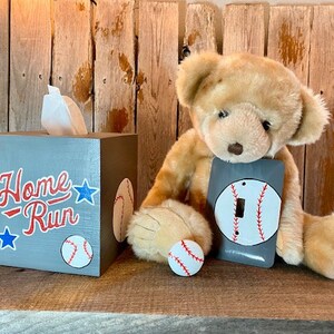 May include: A grey wooden tissue box cover with the words "Home Run" and baseball graphics. A teddy bear is holding a light grey switch plate with a baseball graphic.