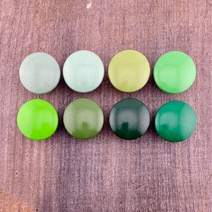 以下が含まれることがあります： 薄い緑から濃い緑まで、さまざまな緑色の丸い木製のボタンが8つあります