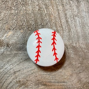 Könnte beinhalten: Ein weiß bemalter Stein mit roten Nähten, der einem Baseball ähnelt.