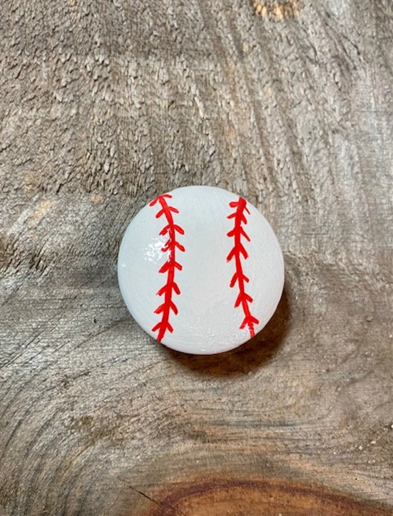 May include: A white painted rock with red stitching, resembling a baseball.