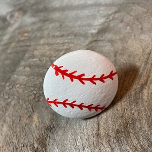 May include: A white painted rock with red stitching, resembling a baseball.