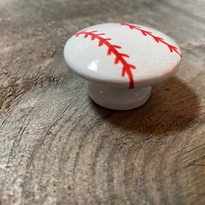 May include: White ceramic cabinet knob shaped like a baseball with red stitching.
