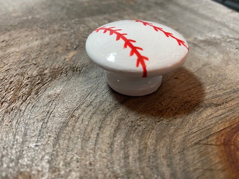 May include: White ceramic cabinet knob shaped like a baseball with red stitching.