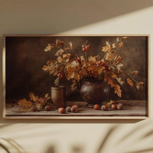 Pu&ograve; includere: Dipinto con cornice di natura morta con un vaso marrone scuro pieno di foglie e bacche autunnali. Una piccola tazza di bronzo &egrave; a sinistra, con ghiande sparse sulla superficie di legno. L'opera d'arte ha un'estetica vintage calda.