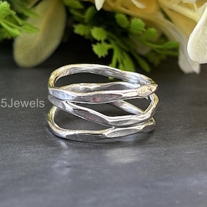 May include: A silver ring with a unique, layered design. The ring features three intertwined bands with a textured, hammered finish. The jewelry is displayed on a dark surface, with the text "925Jewels" visible.