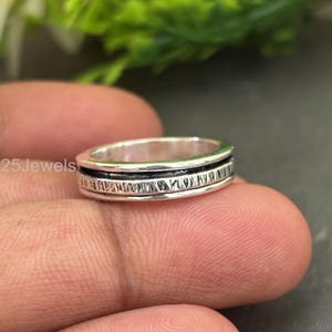 May include: A silver ring with a black band and etched detailing. The ring is shown close-up, with the text "925Jewels" visible in the background. The ring is on a finger.