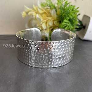 May include: A wide, hammered silver cuff bracelet. The bracelet has a textured surface with small, evenly spaced indentations. The text "925Jewels" is visible on the side. The bracelet is open at the back. A decorative piece of jewellery.