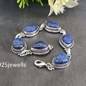May include: A silver bracelet featuring six oval and teardrop-shaped blue lapis lazuli stones. The stones are set in a silver bezel with a rope-like border. The bracelet has a lobster clasp and the text "925jewells".