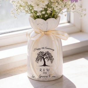 May include: A white ceramic vase filled with a bouquet of pink, yellow, and purple flowers. The vase is decorated with a ribbon and the text "Happy 9th Anniversary", a tree illustration, and the initials "R & W 2026".