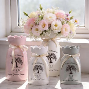 Puede incluir: Cuatro jarrones de cerámica en rosa, blanco y gris, cada uno con una parte superior festoneada y atados con una cinta crema. Los jarrones tienen un gráfico de árbol y el texto "Happy 9th Anniversary 2026 Love Grows Here."