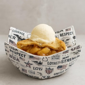 May include: A slice of apple pie topped with vanilla ice cream, served in a patriotic bowl. The bowl is white with a repeating pattern of American flags, stars, and text including "USA", "Respect", and "Loyalty".