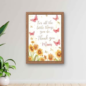 Könnte beinhalten: Ein gerahmter Druck mit einem Aquarelldesign. Das Kunstwerk zeigt Sonnenblumen am unteren Rand, rosa Schmetterlinge und den Text "For all the little things you do, - Thank you, Mom."