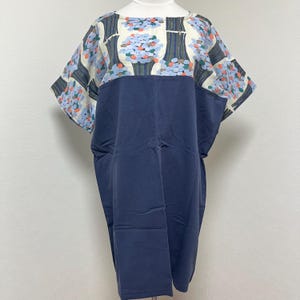 以下が含まれることがあります： ネイビーブルーのドレス、花柄のヨーク付き。ヨークは、クリーム色の背景に青い花と緑の茎のデザインが特徴です。ドレスは半袖で、ゆったりとした快適なフィット感です。