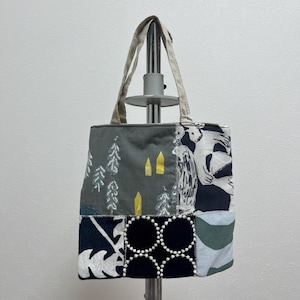 以下が含まれることがあります： さまざまな生地パターンを使用したパッチワークトートバッグ。バッグは森のシーン、白黒の動物柄、その他の幾何学模様が特徴です。ハンドルはニュートラルなベージュ色です。