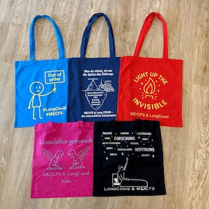 Könnte beinhalten: Eine Sammlung von Tragetaschen in Blau, Marine, Rot, Pink und Schwarz. Jede Tasche zeigt einzigartige Texte und Grafiken zu Long Covid und MECFS. Die Taschen haben lange Griffe.