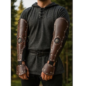 May include: Brown leather arm guards with metal rivets and decorative circular accents. The arm guards are worn over a black long sleeve shirt and are designed to protect the forearms. The medieval-style armor is a dark brown color.