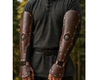 May include: Brown leather arm guards with metal rivets and decorative circular accents. The arm guards are worn over a black long sleeve shirt and are designed to protect the forearms. The medieval-style armor is a dark brown color.
