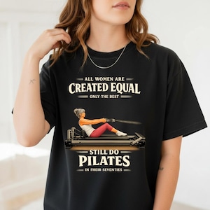 Puede incluir: Camiseta negra con el texto "ALL WOMEN ARE CREATED EQUAL ONLY THE BEST STILL DO PILATES IN THEIR SEVENTIES." La camiseta presenta una ilustración de una mujer haciendo Pilates. La camiseta es de cuello redondo.