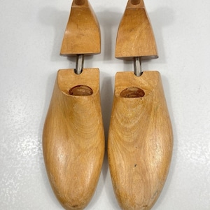 May include: Two wooden shoe trees. Each tree has a rounded toe shape, a wooden heel piece, and a wooden knob at the top. The trees are made of light-colored wood and are designed to maintain the shape of shoes.
