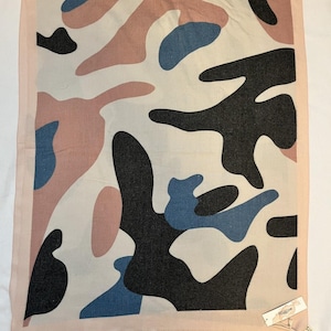 May include: A rectangular scarf with a camouflage pattern in shades of pink, blue, black, and off-white. The scarf has a light pink border and a tag attached to one corner. The fabric appears to be soft and lightweight.