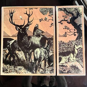 May include: Two rectangular wall art panels featuring a black ink illustration on a light copper-toned background. The left panel depicts a group of deer in a grassy field, while the right panel shows a single deer resting beneath a large tree.