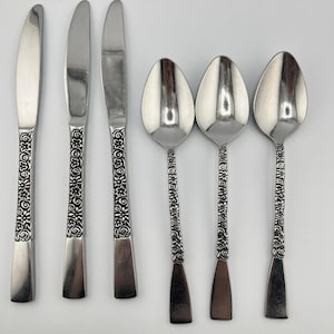 May include: A collection of six silver-coloured cutlery items, comprising three knives and three spoons. The handles are adorned with an intricate floral pattern. The spoons have a rounded bowl, and the knives have a pointed blade.