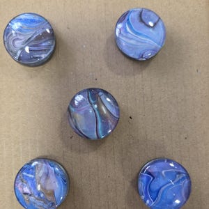 May include: Five round, glass-like objects with swirling blue, purple, and white patterns. The text "Batch 1" is visible at the bottom. The objects have a glossy finish and appear to be decorative.