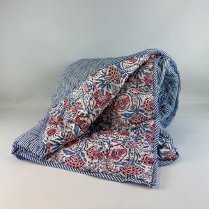 May include: A rolled quilt with a blue and white striped exterior. The interior has a floral pattern with pink and red flowers, blue leaves, and a white background. The quilt is edged with a blue and white striped border.