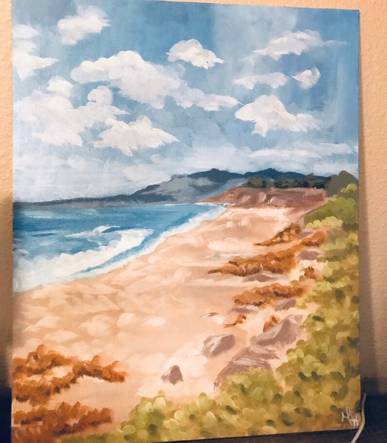 May include: A painting of a beach scene with a blue ocean, white waves, and a sandy shore. The beach is lined with green bushes and brown rocks. The sky is blue with white clouds.