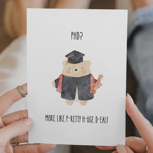 Könnte beinhalten: Eine Grußkarte zum Thema Abschluss. Die Karte zeigt einen Cartoon-Bären mit Doktorhut und Robe, der eine Urkunde hält. Der Text auf der Karte lautet: "PHD? More like P-Retty H-Uge D-Eal!"