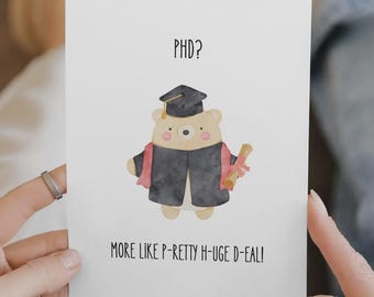 May include: A graduation-themed greeting card. The card shows a cartoon bear in a graduation cap and gown, holding a diploma. The text on the card reads "PHD? More like P-Retty H-Uge D-Eal!"