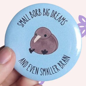 Pode incluir: Um botão azul claro com uma ilustração de um kiwi e o texto "SMALL BORB BIG DREAMS AND EVEN SMALLER BRAIN". O botão tem 5,8 cm de diâmetro.