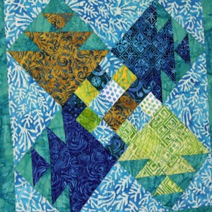 May include: Close-up of a colorful quilt with geometric patterns. The quilt features triangles and squares in shades of blue, green, yellow, and brown. The design includes floral and abstract motifs, creating a vibrant and textured appearance.
