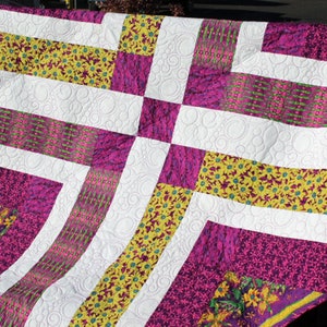May include: A quilt with a patchwork design featuring white, purple, and yellow fabric. The quilt is quilted with a circular pattern.