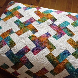 May include: A colorful quilt with a white background and a repeating pattern of interwoven rectangles in shades of blue, green, orange, and purple. The quilt has a quilted design.