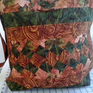 May include: A quilted brown, green, and pink fabric tote bag with a brown strap. The bag has a patchwork design with a swirl pattern.