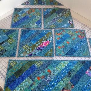 May include: Set of six blue and green quilted placemats with a diagonal pattern. The placemats are made from fabric scraps and have a variety of different patterns and colors.
