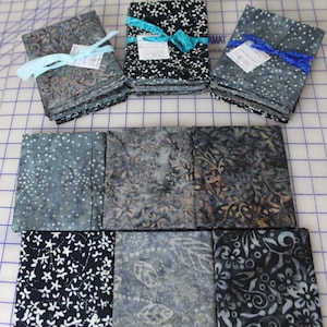 May include: Stacks of fabric bundles in various patterns and colors, including floral and dotted designs. The bundles are tied with ribbons in shades of blue. The fabrics appear to be cotton or a similar material, suitable for quilting or crafting projects.