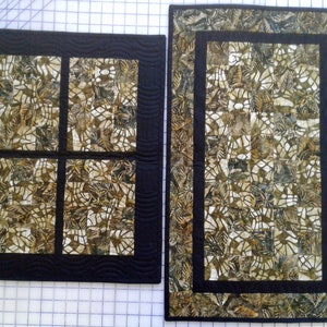 May include: Two quilted wall hangings with a black background and a brown and white patterned design. The smaller hanging is divided into four squares.