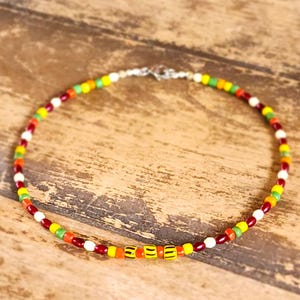 May include: A colorful beaded necklace with a silver clasp. The necklace features a variety of small, round beads in shades of red, orange, yellow, green, and white. The beads are strung together to create a vibrant and eye-catching accessory.